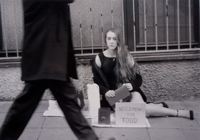Eine Frau in einem Abendkleid sitzt auf der Strasse und bettelt.